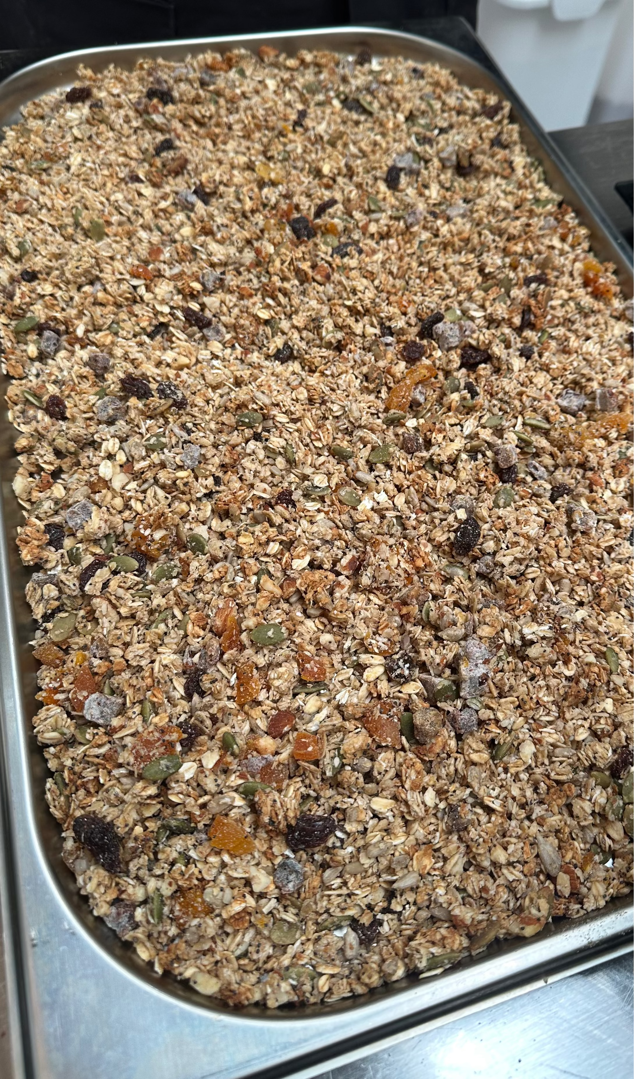 Baking tray filled with freshly baked Artisan Granola, showing golden oats, nuts, seeds and dried fruit cooling after being baked in small batches.
