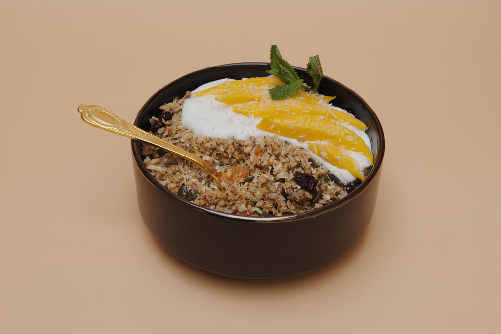 Artisan Granola breakfast bowl with yoghurt, fresh mango slices, mint garnish and a gold spoon — a wholesome, high-fibre, handmade granola served with fruit for a healthy and indulgent breakfast.