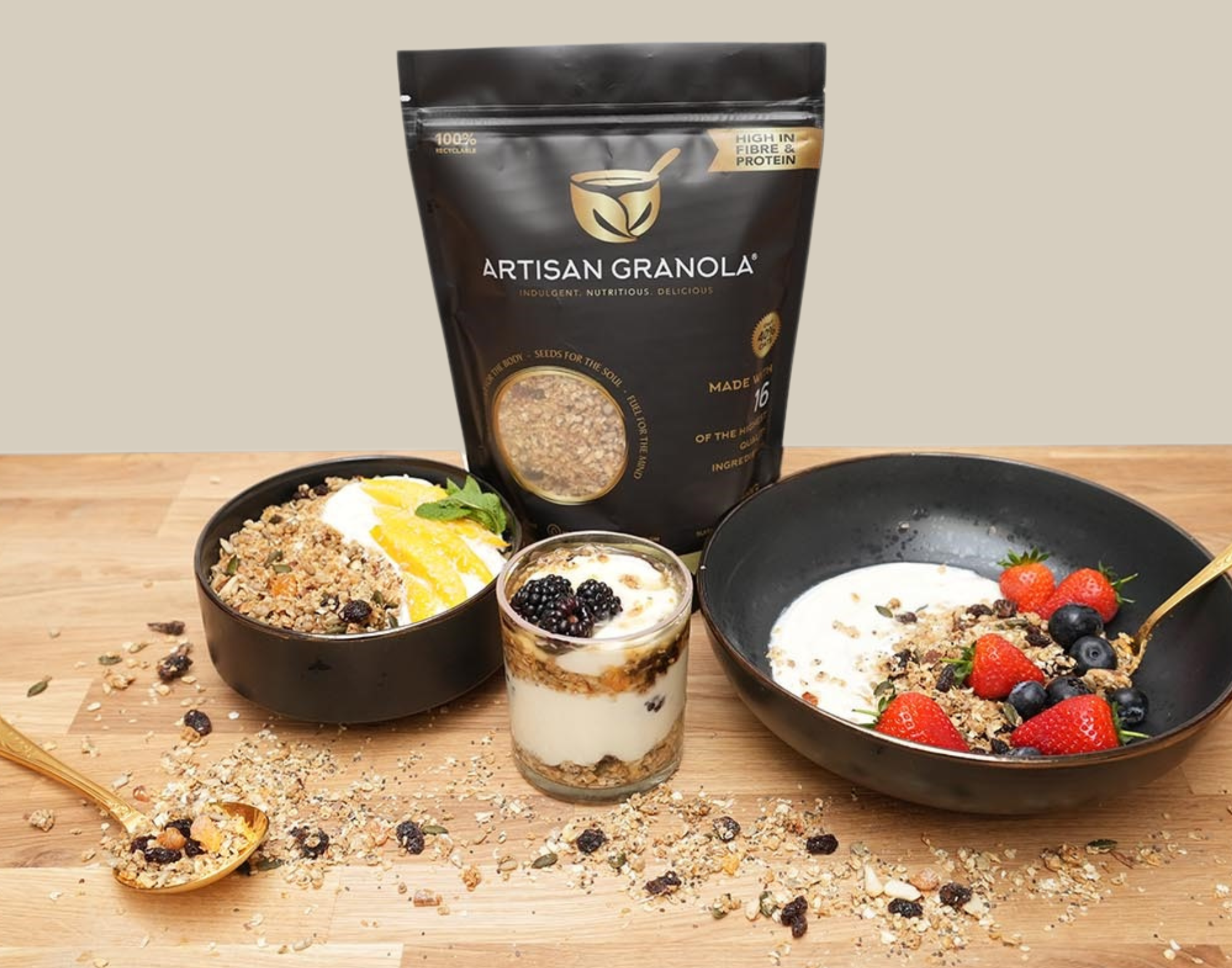 Artisan Granola luxury breakfast display featuring a black pouch of handmade granola with bowls of yoghurt, granola, fresh strawberries, blueberries, blackberries and orange slices on a wooden table — healthy, high-fibre natural breakfast option. 
