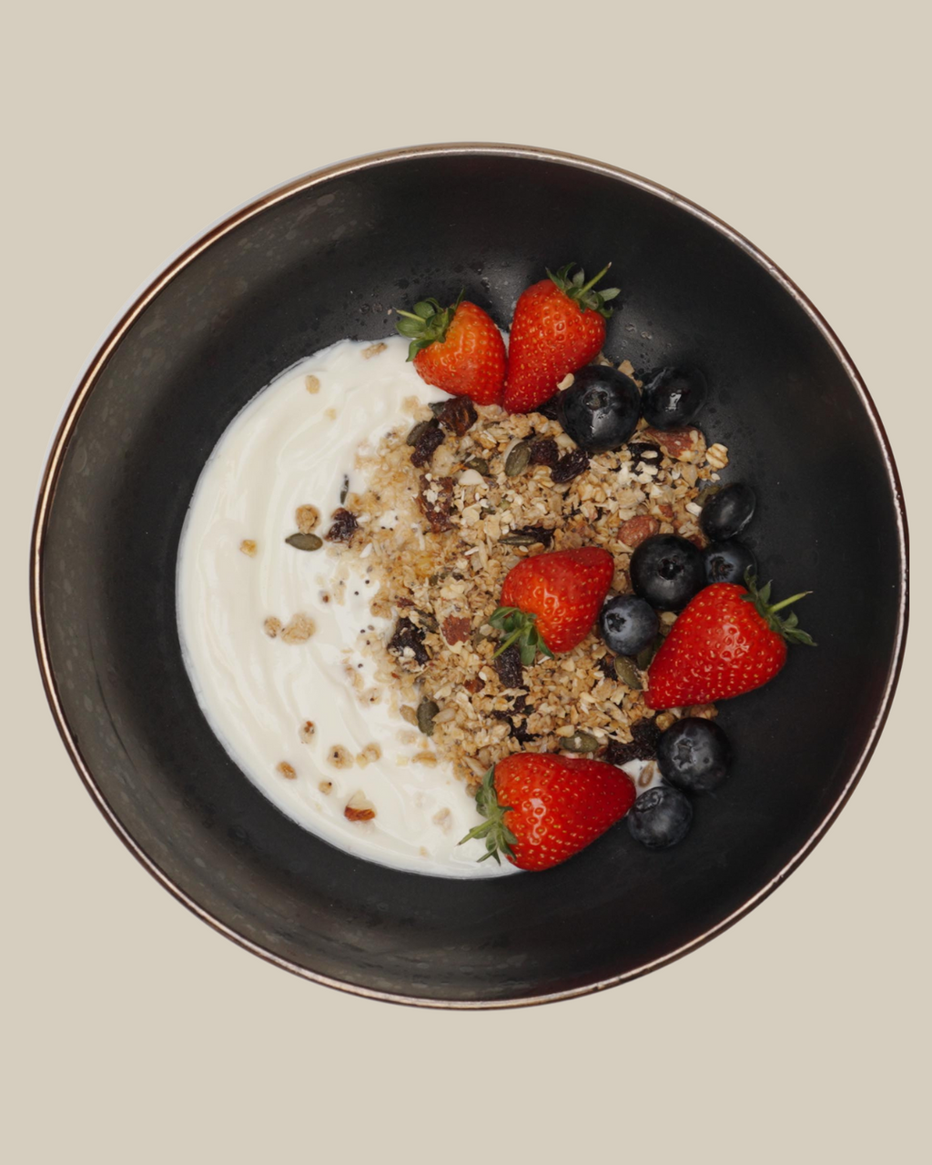 Artisan Granola served with creamy yoghurt, fresh strawberries and blueberries in a black bowl — a healthy, high-fibre breakfast made with natural, handmade granola. 